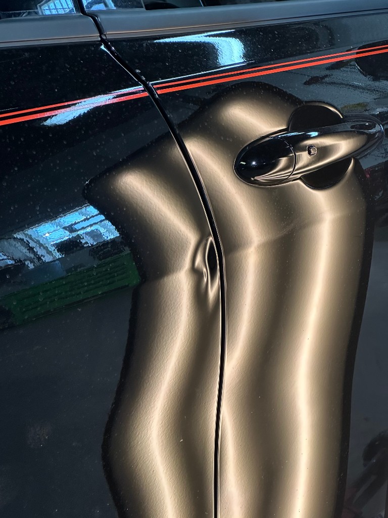 Before PDR: black sedan door with red pinstripes, vertical crease dent near door edge
